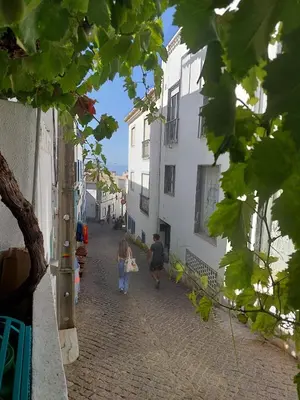 two people walking down a cobblestone street with buildings at Casa da Praia Burgau in Burgau
