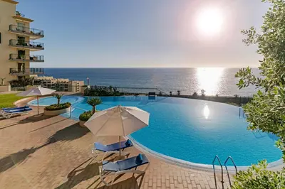 a swimming pool with chairs and umbrellas and the ocean at Vila Formosa III by An Island Apart in Funchal