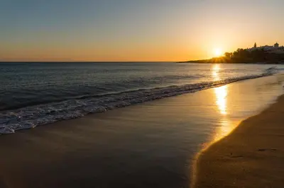 a beach at sunset with the sun setting over the ocean at Apartment do Ramses in Luz