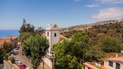 a white building with a clock tower on a hill at Mill House in Ponta do Sol