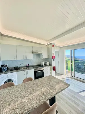 a kitchen with white cabinets and a table with chairs at Hera House, Ponta do Sol, Portugal in Canhas