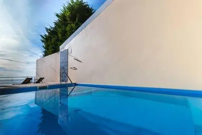 a blue swimming pool with a white wall at Cozy Private Apartment Calheta in Arco da Calheta