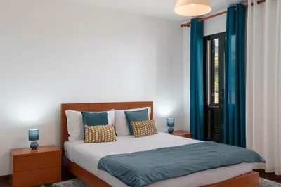 a bedroom with a bed with blue curtains and a window at Palmasol by An Island Apart in Calheta