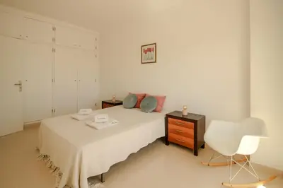 a white bedroom with a bed and a chair at FLH Budens Duplex with Terrace in Vila do Bispo