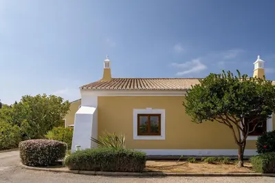 a small yellow house with a tree and bushes at 2 bdr Villa with Ocean-View Shared Pool, Luz, Lagos in Luz