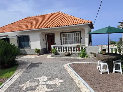 a small house with a table and an umbrella at Casa Sequeira in Fajã da Ovelha