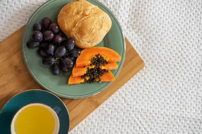 a plate of food with fruit and a roll and a cup of juice at Rumo by KAAMAH in Ribeira Brava
