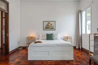 a white bedroom with a large white bed and two windows at Rumo by KAAMAH in Ribeira Brava