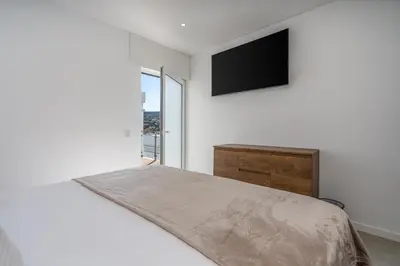 a white bedroom with a bed and a flat screen tv at Aurazul Apartment in Luz