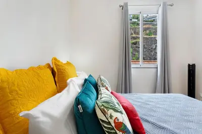 a bedroom with a bed with colorful pillows and a window at Moradia Centro Da Cidade Funchal in Funchal