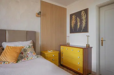 a bedroom with a bed and a yellow dresser at Jardim do Caniço in Caniço