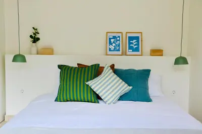 a white bed with green and blue pillows on it at Araça Studio - Atlantic Mountain Living in São Vicente