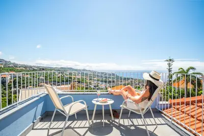 a woman sitting on a balcony with a glass of wine at The Vinehill House in Câmara de Lobos
