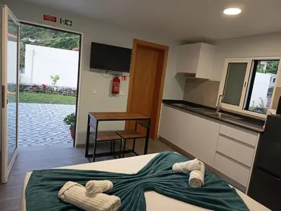 a room with a bed and a kitchen with slippers at Pousada Teixeira 11C in São Vicente
