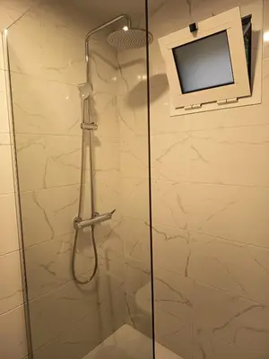 a bathroom with a shower with a television on the wall at Pousada Teixeira 11C in São Vicente