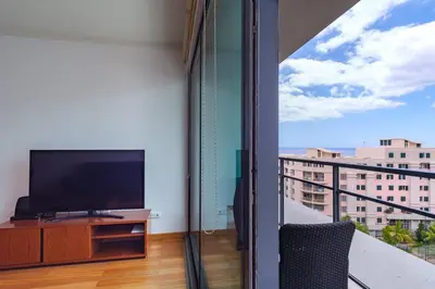 a living room with a tv and a balcony at GuestReady - Modern space close to Formosa Beach in Funchal