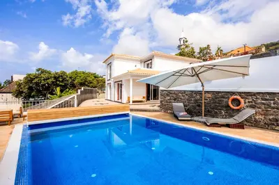 a swimming pool with an umbrella next to a house at Villa Crossdeira - A Wellness Retreat in Arco da Calheta