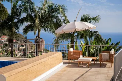 a balcony with chairs and an umbrella and a pool at Villa Crossdeira - A Wellness Retreat in Arco da Calheta