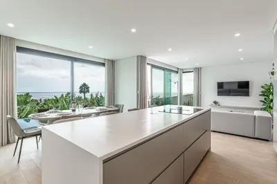 a kitchen with a large white island and a living room at Eco Fajã Villas in Arco da Calheta