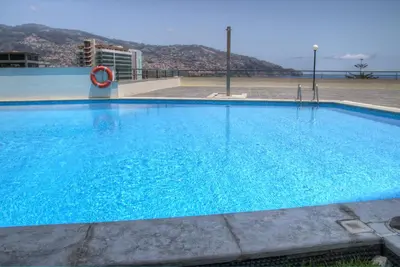 a large blue swimming pool with a mountain in the background at Monumental Apartment in Funchal