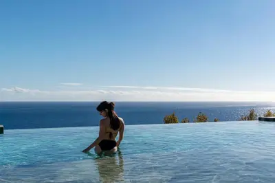 a woman in a swimming pool with the ocean in the background at Savoy Monumentalis VII by An Island Apart in Funchal