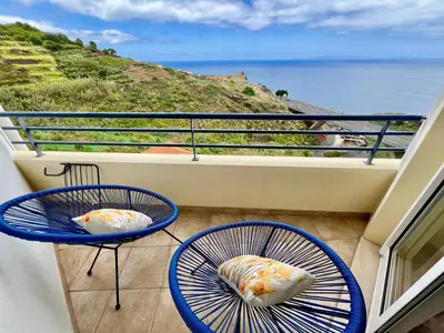 two blue chairs on a balcony with a view of the ocean at Maria do Mar Apartment in Caniço