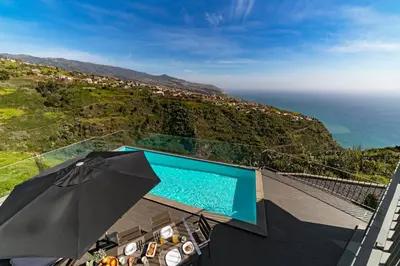 an umbrella and chairs next to a swimming pool at Villa Clementina | Cliffs&Ocean | Heated Pool in Prazeres