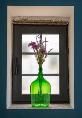 a green vase with purple flowers in a window at The Yellow Cottage Nature House São Vicente Madeira Island in São Vicente