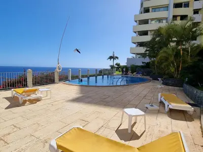 a swimming pool with chairs and a building and the ocean at A Dream on the Cliff in Funchal