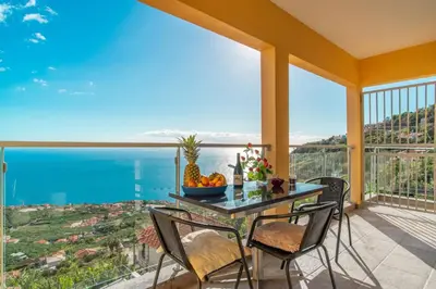 a table and chairs on a balcony with a view of the ocean at Villa Casanova in Arco da Calheta