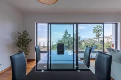 a dining room with a glass table and chairs and a balcony at Sea View Apartment in Caniço