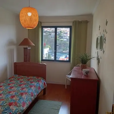 a bedroom with a bed and a table and a window at Apartamento Silvestre Freitas in Funchal