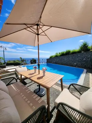 a table with an umbrella next to a swimming pool at Villa Ocean Wave Calheta - Oversized Pool & Stunning Ocean Views in Calheta