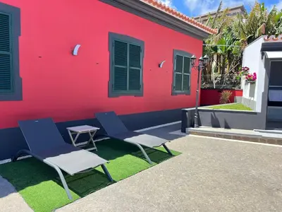 two chairs and a table in front of a red building at Studio Refúgio in Ponta do Sol