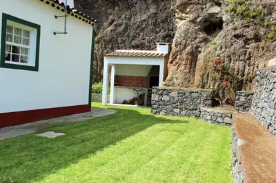 a house next to a rock wall with a yard at Casa da Avó - Turismo Rural in Santo Espírito