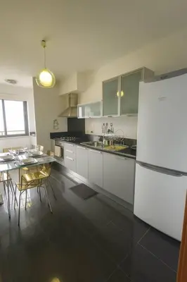 a kitchen with white cabinets and a table and a refrigerator at Alojamiento Local - Nilia in Caniço