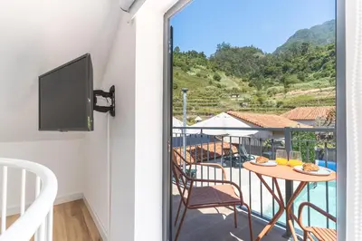 a room with a balcony with a table and a tv at Avo Maria 2 House by AH in São Vicente