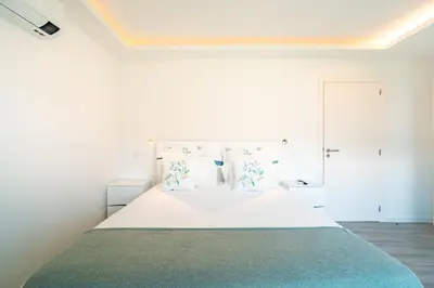 a white bedroom with a large bed with white sheets at Vilaugusto in São Vicente