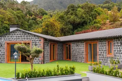 a stone house with a green lawn and trees at Vilaugusto in São Vicente