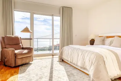 a bedroom with a bed and a chair and a large window at Ponta do Sol Sea View, a Home in Madeira in Ponta do Sol