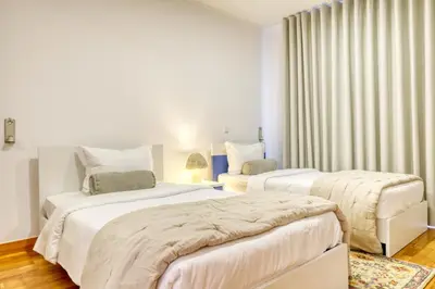 a white bedroom with two beds and a chair at Ponta do Sol Sea View, a Home in Madeira in Ponta do Sol