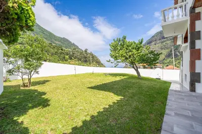 a grassy yard with a white wall and trees at Casa do Vale in São Vicente