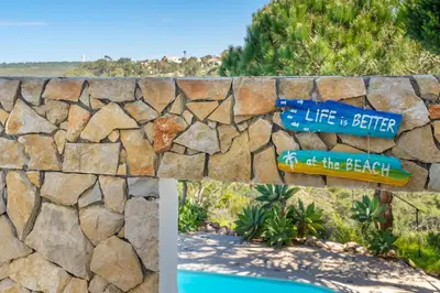 a stone wall with a sign that reads life is better at the beach at Duas Palmeiras in Aljezur