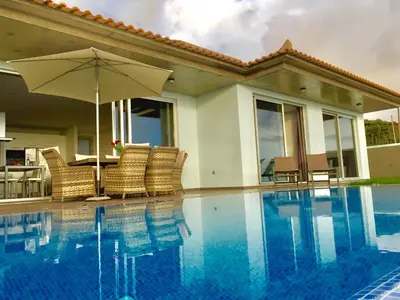 a swimming pool with chairs and an umbrella next to a house at Villa Pinheira III heated pool in Calheta
