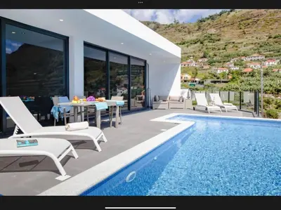 a villa with a swimming pool with chairs and a table at Villa Rubydom by Turin in Arco da Calheta