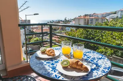 a table with croissants and orange juice on a balcony at Sol Garajau Apartment by Atlantic Holiday in Santa Cruz