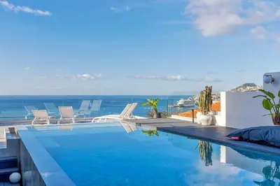 a swimming pool with chairs and the ocean in the background at Villa Lázaro By Holiday Rental Madeira in Funchal