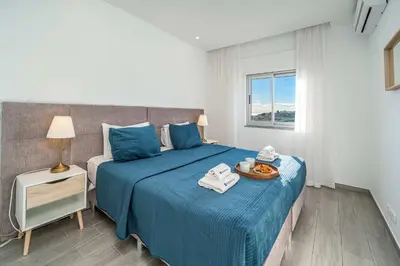a bedroom with a bed with blue sheets and a window at Beachfront Flat & Panoramic Sea View by HostWise in Luz
