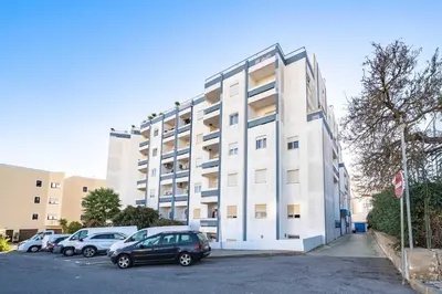 a white building with cars parked in a parking lot at Beachfront Flat & Panoramic Sea View by HostWise in Luz