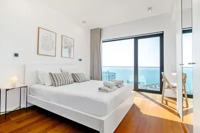 a white bedroom with a large bed and a large window at Ocean Vista- T2 Funchal in Bicas
